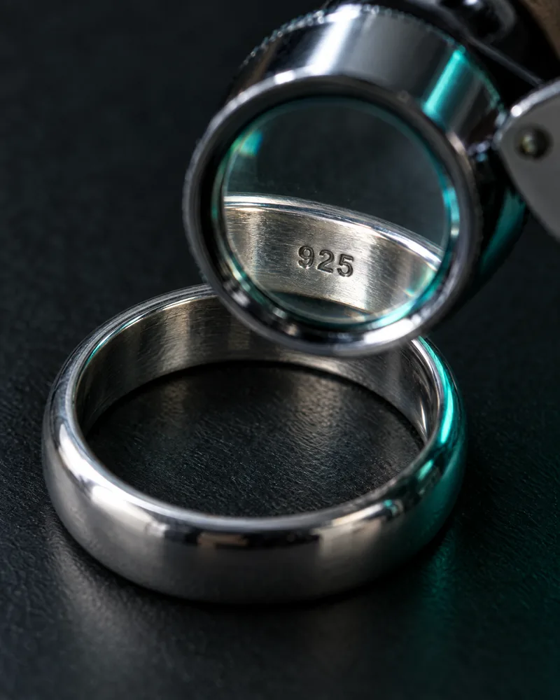 Illustration of the inside of a plain silver ring band with a generic 925 mark under a magnifying loupe